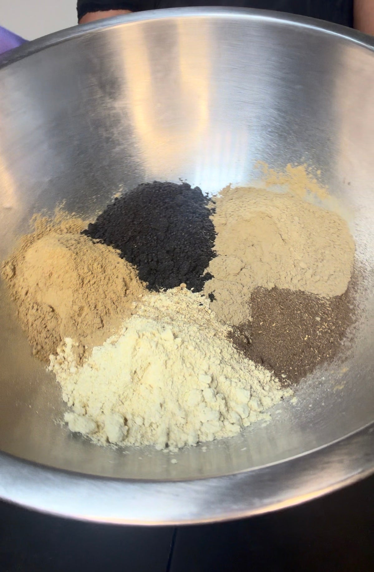 Stainless bowl filled with mixed herbal powders and seed blends for hair treatment